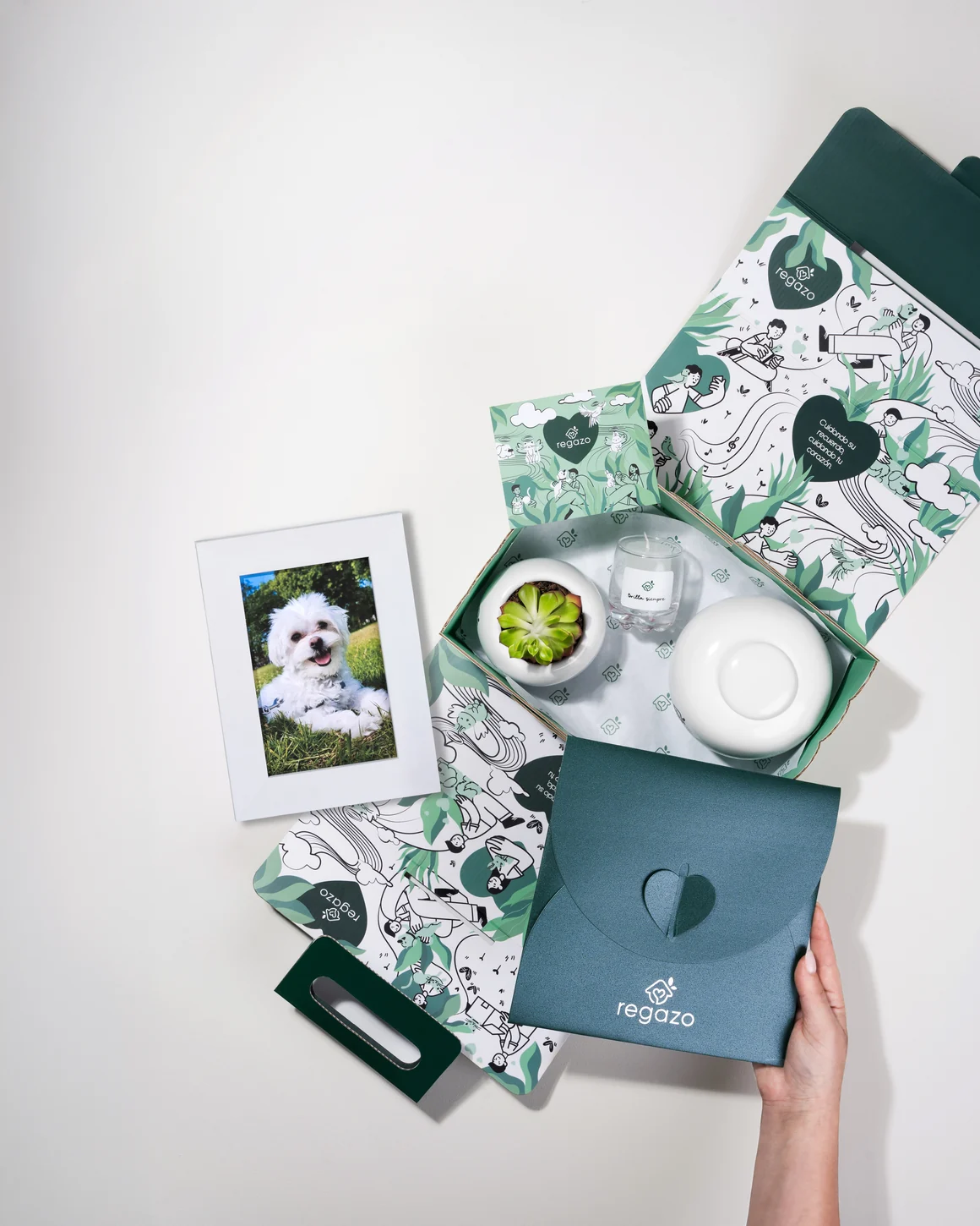 Homenaje completo de Regazo recién abierto, con su urna de cerámica, el cuadro con la foto de la mascota, la maceta con planta, la vela y la carta en su sobre
